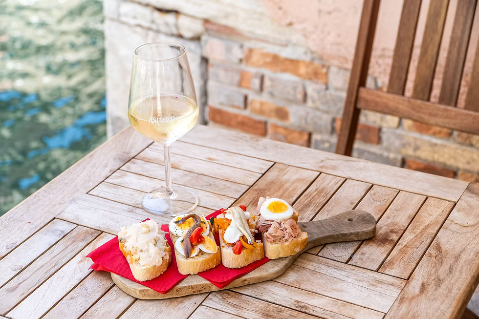 Cicchetti veneziani su tagliere con un calice di vino bianco